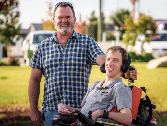 photo of two men. one is standing, the other in a wheelchair