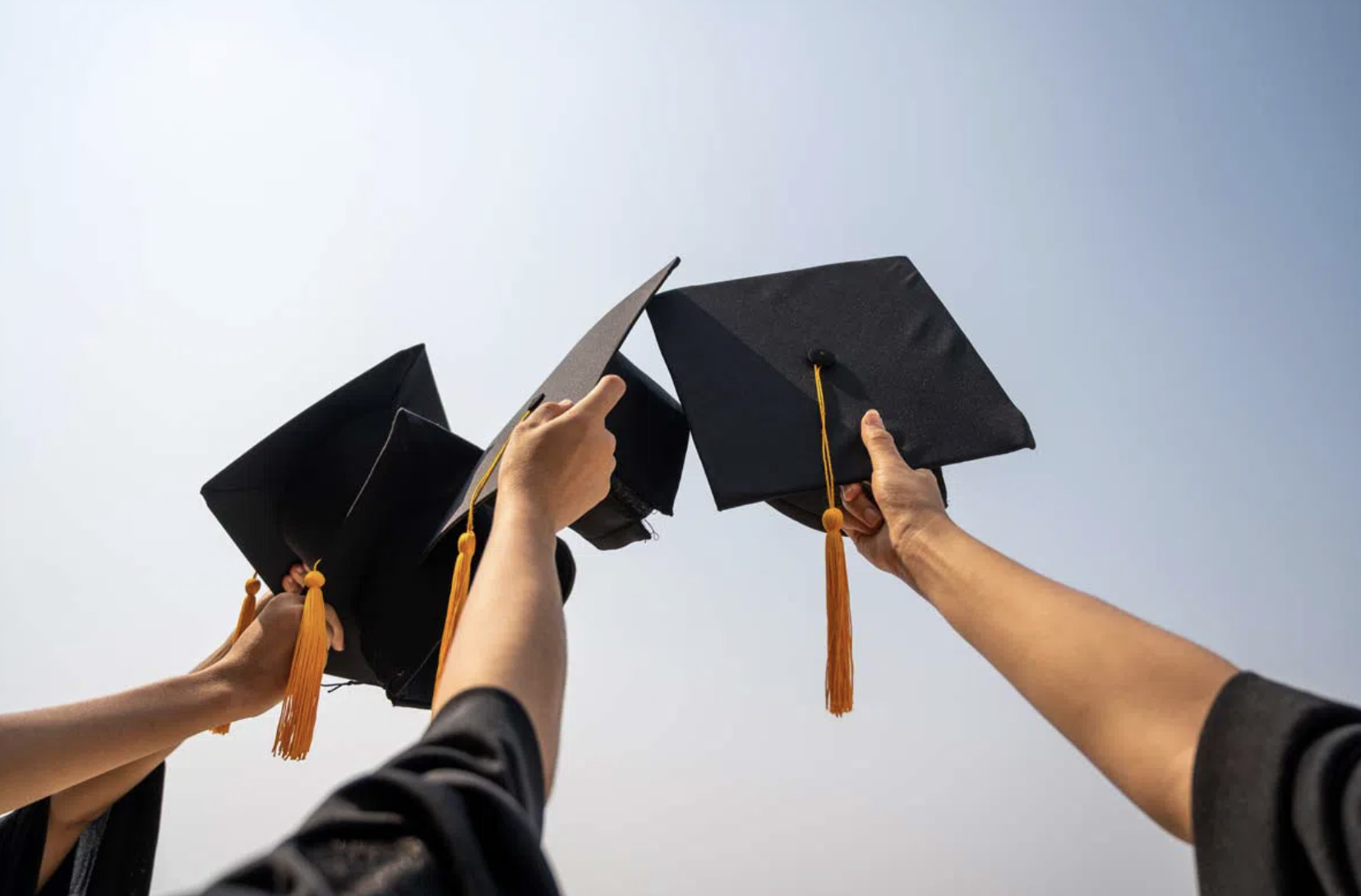 photo of three arms holding up three graduation caps
