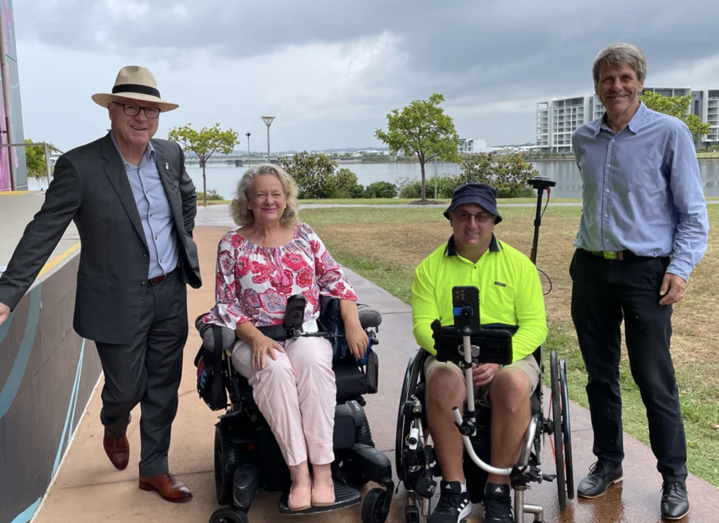 photo of four smiling people - two are standing, two in wheelchairs